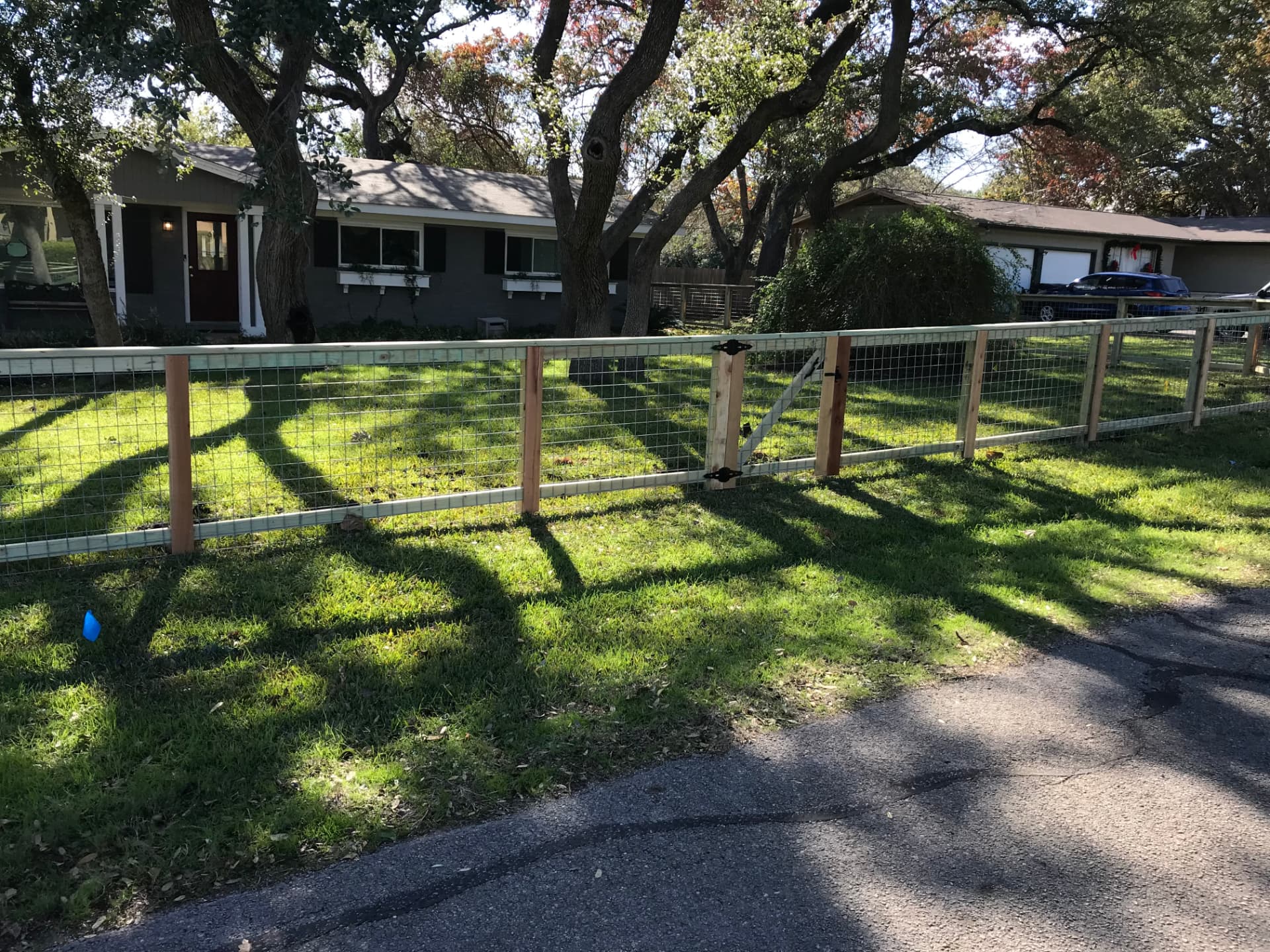 Wire and wood perimeter fence with a gate around a sunny residential lawn